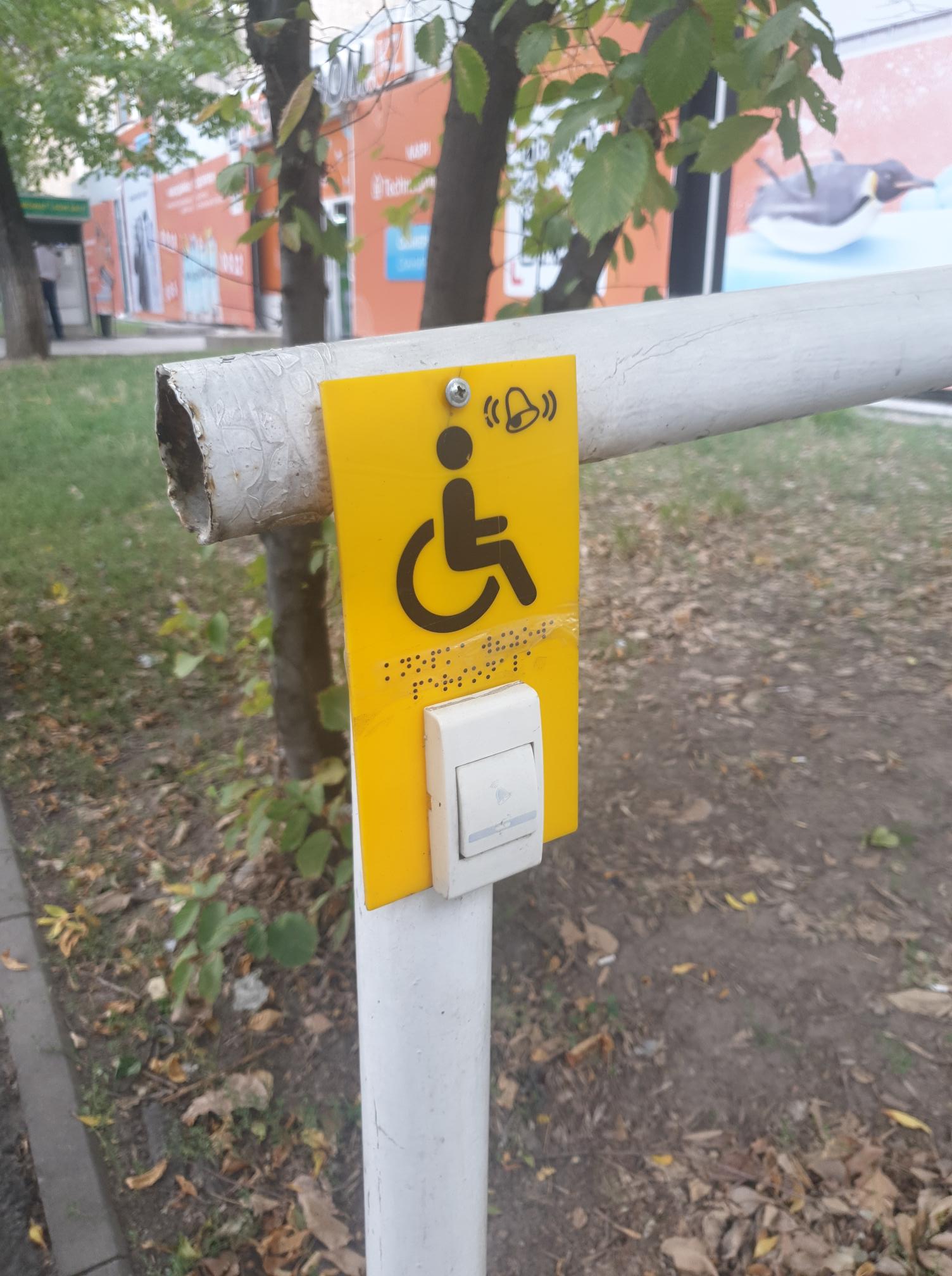 kuvassa keltainen kyltti, jossa on pyörätuolisymboli ja kutsunappi.